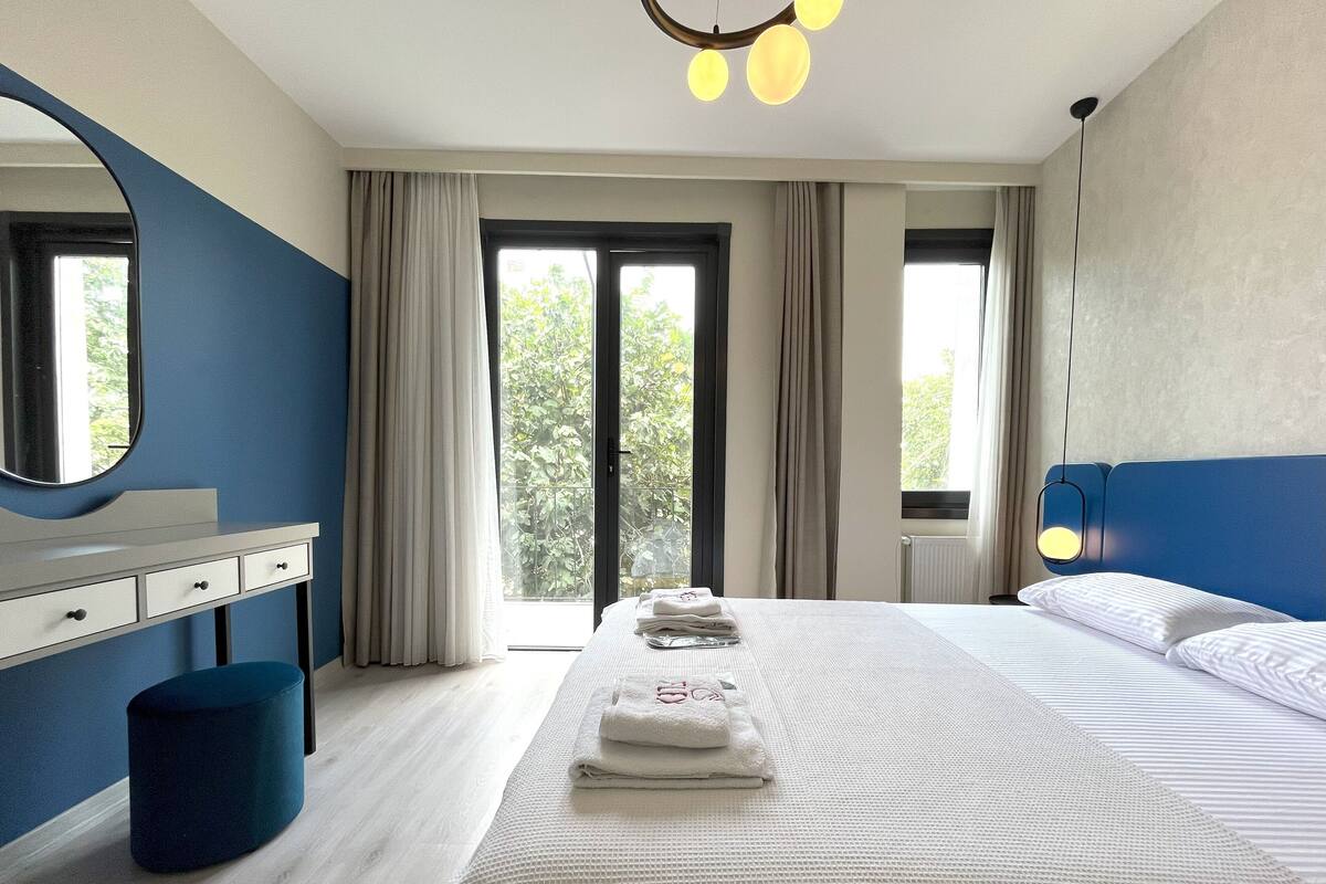 Habitación de hotel moderna con una cama grande, una mesita de noche, un espejo y vistas a zonas verdes.