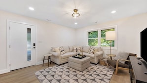 A modern living room with a beige sofa set, a coffee table, a side table, a lamp, and a TV stand. - {Renovated 2BR in CLT – Where Location, Comfort & Mild Bragging Rights Collide} (Charlotte)