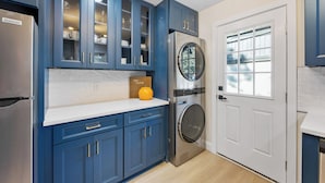 A kitchen with blue cabinets, a stainless steel refrigerator, a washing machine, and a white door with a window. - {Renovated 2BR in CLT – Where Location, Comfort & Mild Bragging Rights Collide} (Charlotte)