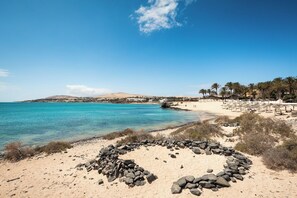 A beach with a heart-shaped rock formation, clear turquoise water, and a distant mountain. - Home2Book Modern Apt with Pool in Corralejo Oasis (Corralejo)