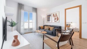 Un salon moderne avec un canapé, une table basse et un téléviseur posé sur une console blanche.