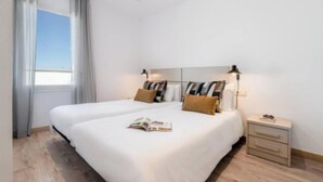 Une chambre d’hôtel avec deux lits, une table de chevet avec une lampe et une fenêtre avec des rideaux.