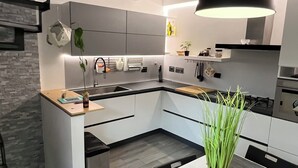 A modern kitchen with a central island, a dining area with a table and chairs, and a hanging pendant light.