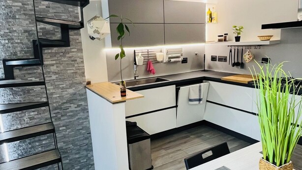 A modern kitchen with a central island, a dining area with a table and chairs, and a staircase with a unique design.