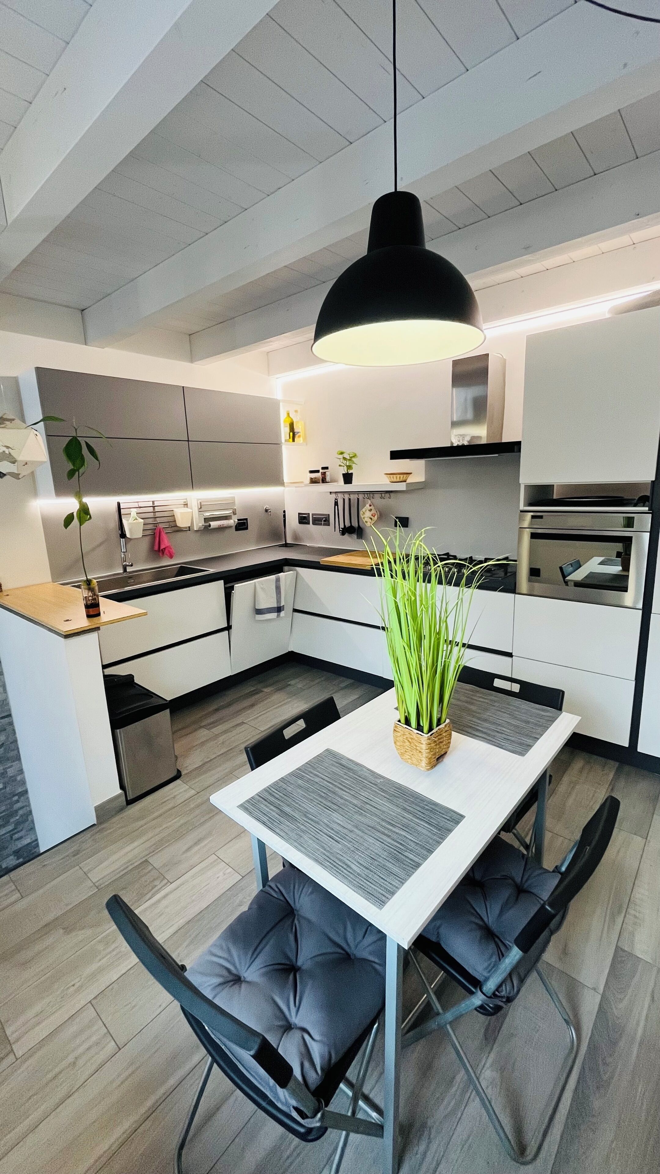 Une cuisine moderne avec un coin repas, comprenant un îlot central, des chaises noires et un luminaire suspendu.