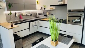 A modern kitchen with a dining area, featuring a central island, black chairs, and a hanging light fixture.