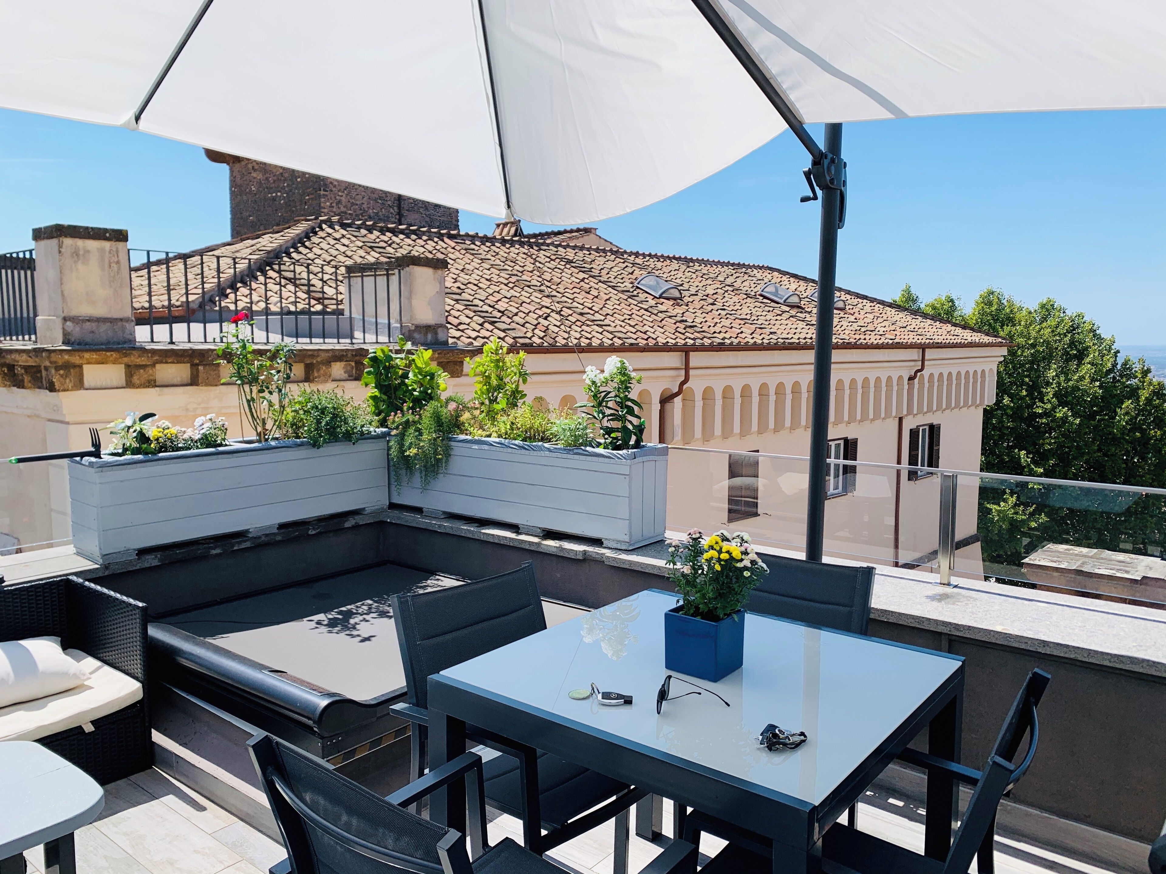 An outdoor patio with a glass table, black chairs, and a white umbrella.