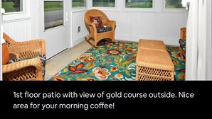 Eine Terrasse im ersten Stock mit Blick auf einen Golfplatz. Sie ist mit Korbmöbeln und einem bunten Teppich ausgestattet.