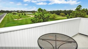 Ein Balkon mit Blick auf einen Golfplatz, einem weißen Geländer und einem runden Tisch.