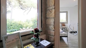 Une pièce avec un mur en pierre, une fenêtre donnant sur un paysage verdoyant, une petite table avec un vase de fleurs et un panneau avec du texte.