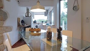 Une cuisine moderne dotée d’une grande fenêtre, d’un luminaire suspendu et d’un coin repas avec une table et des chaises en verre.