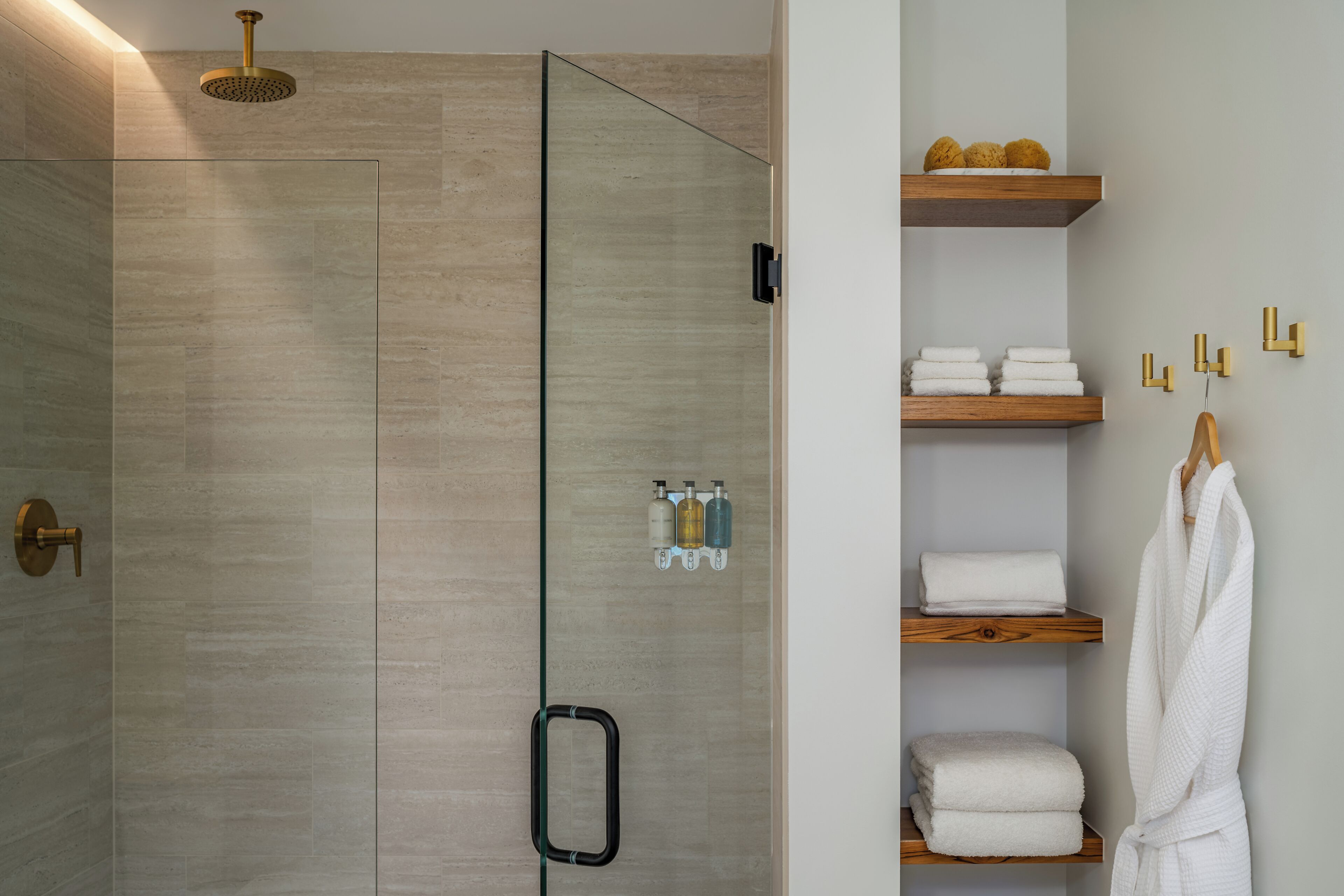 A modern bathroom with a glass shower enclosure, a towel rack, and a shelf with toiletries.