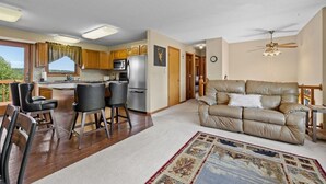 Un espacio habitable amplio con un sofá de cuero, una zona de comedor con taburetes de bar, una cocina con refrigerador y un ventilador de techo.