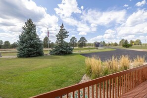 A grassy area with a paved path, a wooden deck, and a flagpole with an American flag.