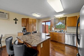 A kitchen with a granite countertop, wooden cabinets, a stainless steel refrigerator, and a dining area with chairs.