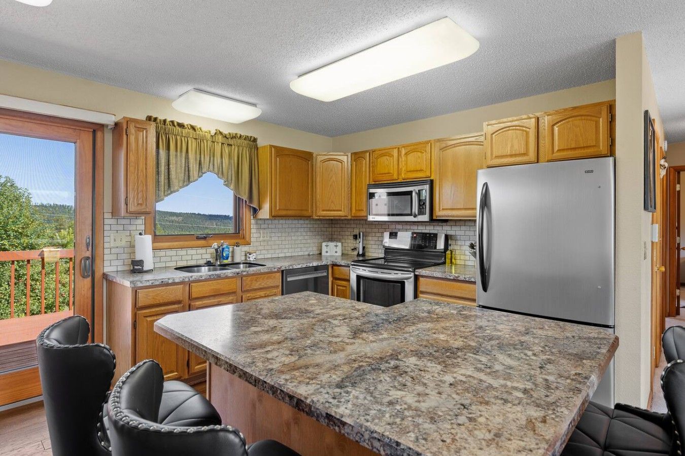 A kitchen with granite countertops, wooden cabinets, stainless steel appliances, and a view through a window.