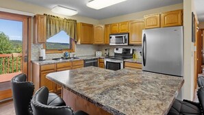 Una cocina con encimeras de granito, armarios de madera, un refrigerador de acero inoxidable y un microondas.