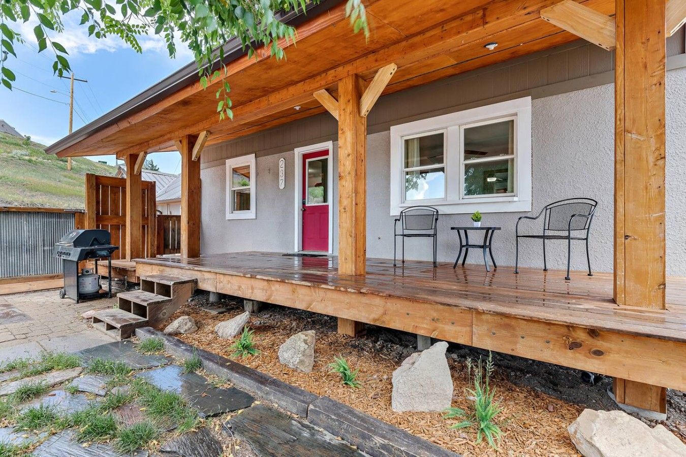 A wooden deck with outdoor seating, a grill, and a red door.