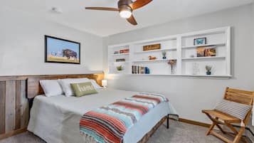 Un dormitorio con cama, ventilador de techo, estantería y una silla.