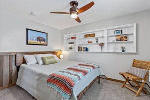 Ein Schlafzimmer mit einem Bett, einem Deckenventilator, einem Bücherregal und einem Sessel.
