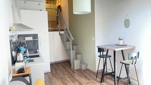 Ein kleiner Wohnbereich mit Küchenzeile, einem Essbereich mit Tisch und Stühlen, einer Treppe und einer Hängelampe.
