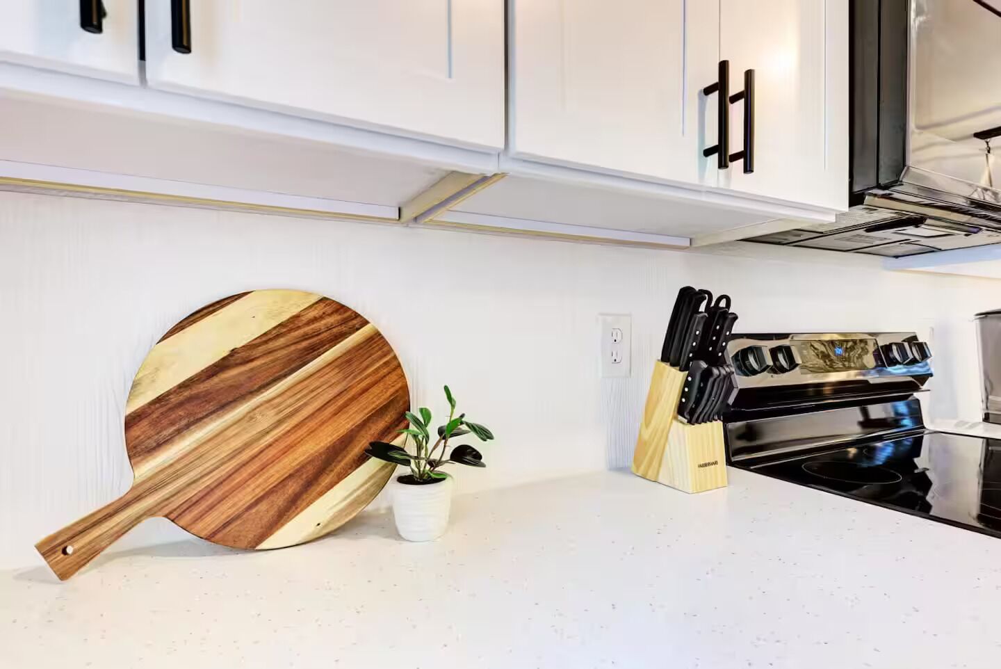 A kitchen with white cabinets, a wooden cutting board, a potted plant, and a knife block.