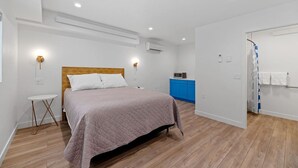 Un dormitorio con cama, mesitas de noche, un escritorio pequeño, un armario azul y zona de ducha.