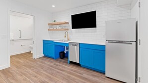 Una cocina moderna con armarios blancos y azules, lavavajillas integrado y refrigerador blanco.