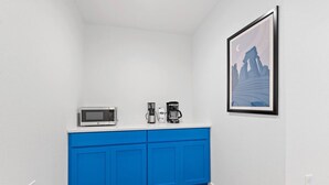 Una cocina pequeña con un microondas blanco, una cafetera y un cuadro en la pared.