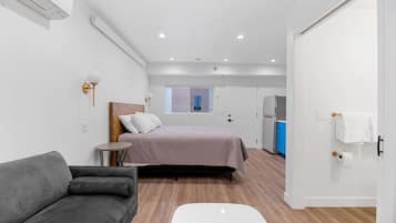 Une pièce de taille modeste comprenant un lit, une petite table, un canapé, une fenêtre et un coin cuisine.