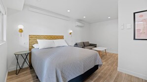 A modern hotel room with a bed, a small table, a sofa, and wall-mounted lighting. - Queen City Inn and Extended Stay #2 (Spearfish)