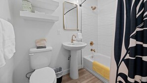 A modern bathroom with a toilet, sink, and shower. There are shelves above the toilet and a mirror above the sink. - Queen City Inn and Extended Stay #2 (Spearfish)