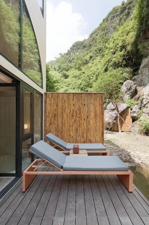 Una terraza con dos sillones y una mesa, rodeada por un cerco de madera, con vistas a un paisaje montañoso.
