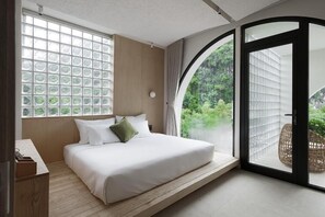 Ein Schlafzimmer mit Bett, einem Fenster mit Blick auf Grünflächen und einer Schiebetür zu einem Außenbereich.