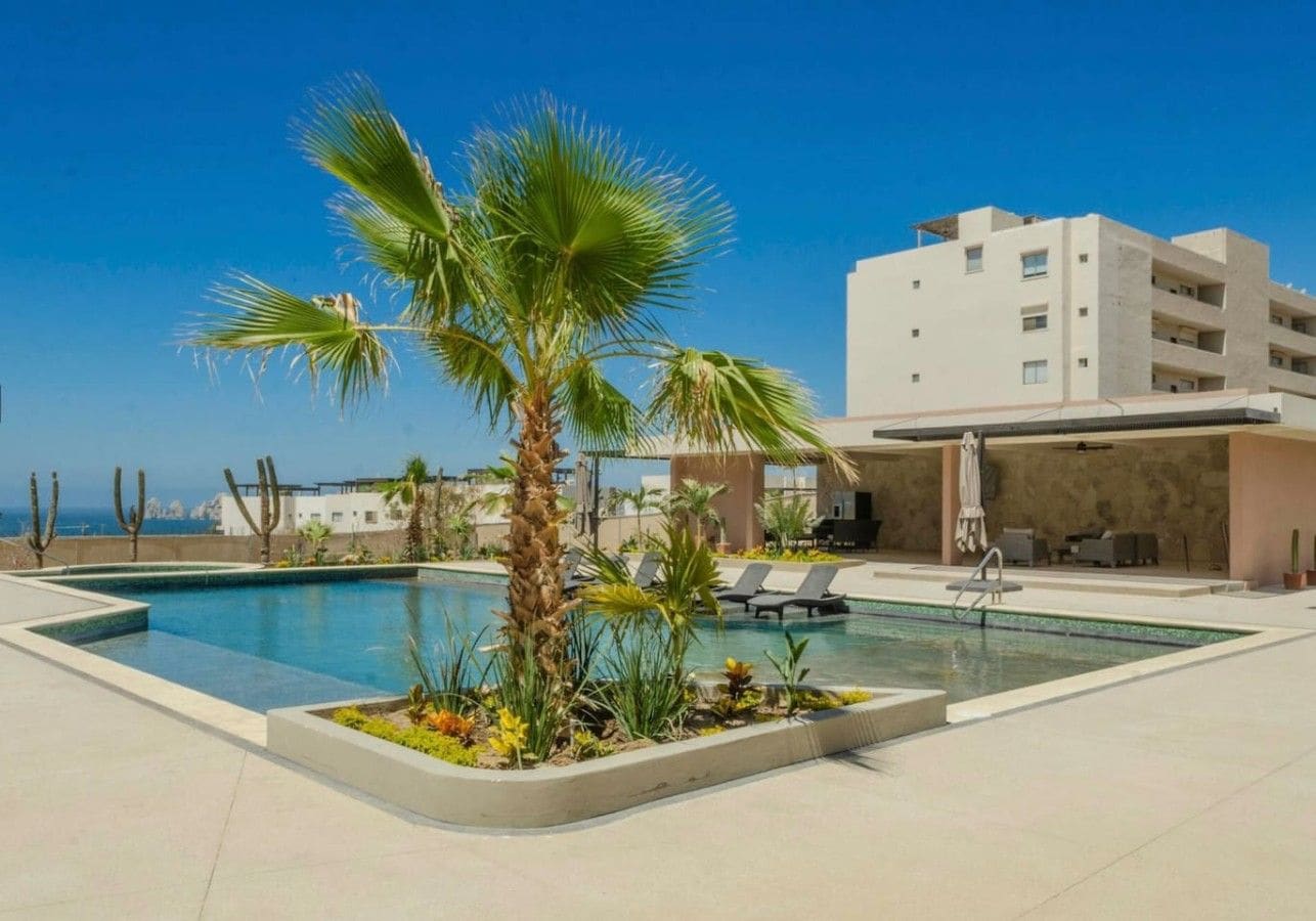 A swimming pool with palm trees, lounge chairs, and a building with balconies.