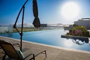 A clear sky, a swimming pool, a lounge chair, and a partial view of a building with the name 'Soriana' on it. - Modern 2BR with Ocean Views (Cabo San Lucas)