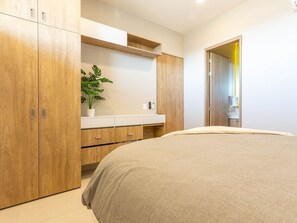 A bedroom with a large bed, wooden wardrobe, and a white bedside table with a plant. - Modern 2BR with Ocean Views (Cabo San Lucas)