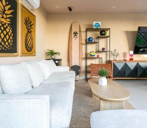 A modern living room with a sofa, a coffee table, a surfboard, and a TV.
