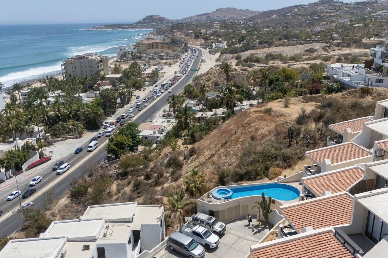 Zona residencial costera con una carretera, piscina y edificios con tejas rojas.