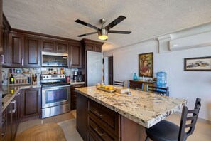 A kitchen with dark wood cabinets, stainless steel appliances, a granite countertop, and a ceiling fan.