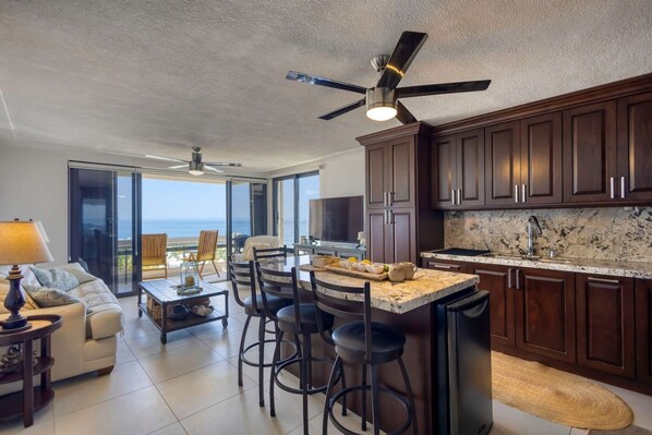 A modern kitchen with dark wooden cabinets, a marble countertop, and a ceiling fan.