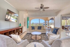 A spacious living room with a sofa, armchairs, a coffee table, and a TV mounted on the wall.