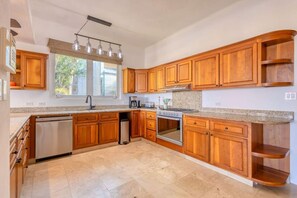 A kitchen with wooden cabinets, a dishwasher, a stove, and a window with a view of greenery.
