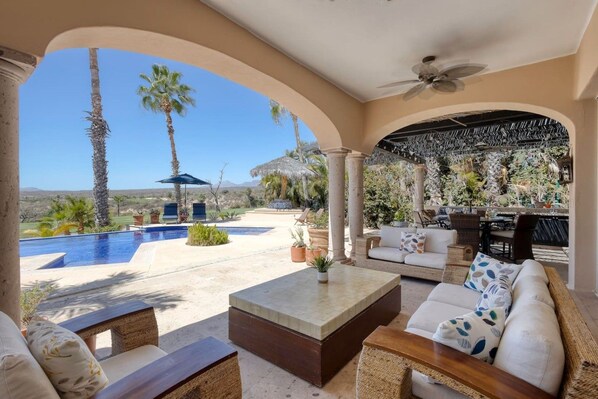 A covered outdoor area with a pool, seating, and a view of the landscape.