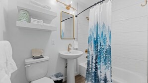 Un baño con inodoro, lavamanos y cortina de ducha con diseño de bosque.