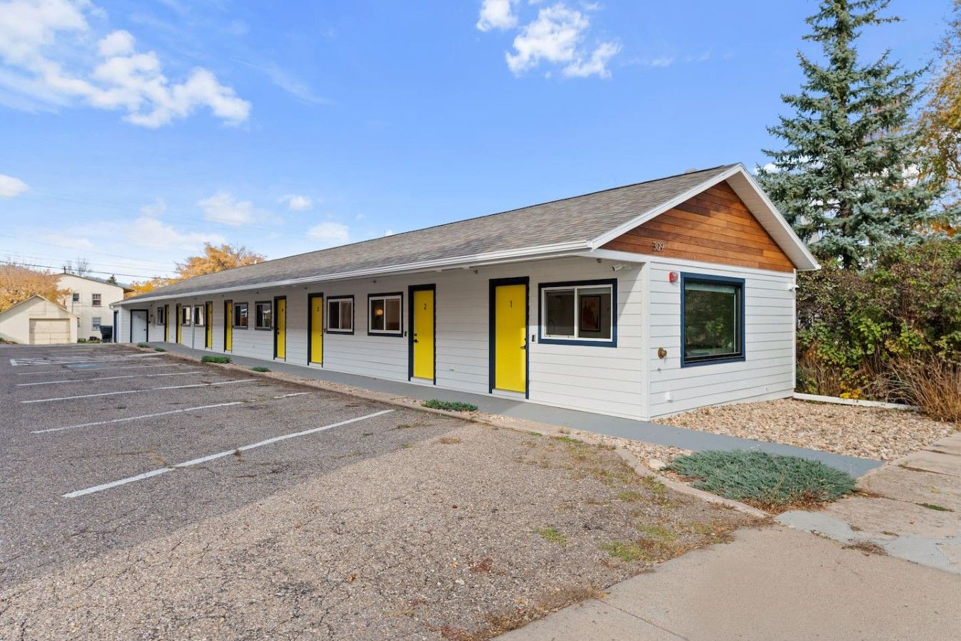 A motel with a row of rooms, a parking lot, and a small garden area.
