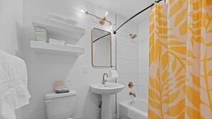 A bathroom with a toilet, sink, and shower. There are towels and toiletries on shelves. - Queen City Inn and Extended Stay #6 (Spearfish)