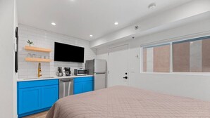 Un dormitorio con una cama, una kitchenette pequeña con microondas, cafetera y televisor.