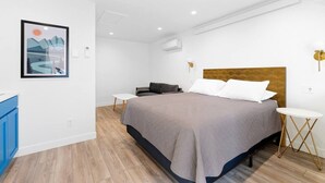Un dormitorio moderno con una cama grande, una mesita, un sofá y aire acondicionado instalado en la pared.