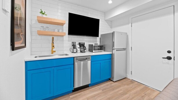 Una cocina moderna con armarios blancos y azules, un lavavajillas de acero inoxidable, un microondas, una cafetera y un refrigerador.